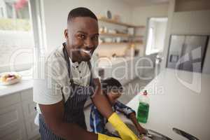 Smiling father and son cleaning utensils in kitchen