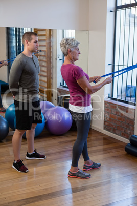 Male physiotherapist helping patient in performing exercise with resistance band