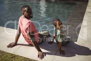 Smiling father and son sitting on edge of swimming pool
