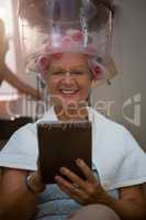 Smiling senior woman using digital tablet while sitting under hair steamer