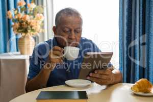 Senior man using digital tablet at table in nursing home