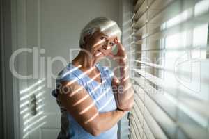 Tense senior woman standing near window in bedroom