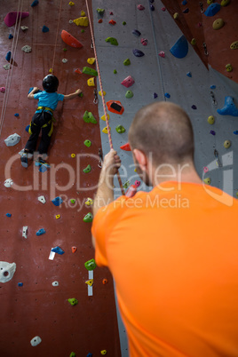 Trainer assisting boy in rock climbing