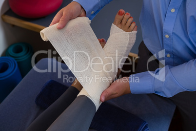 Physiotherapist putting bandage on injured feet of patient