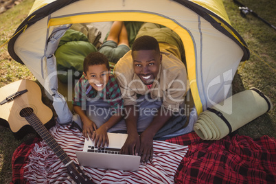 Smiling father and son using laptop in tent