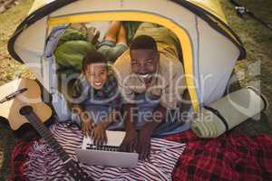 Smiling father and son using laptop in tent