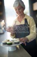 Senior woman picking up the cupcake from the tray