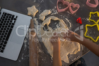 Cropped hands of girl making shape on dough at kitchen counter