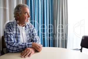 Thoughtful senior man sitting at table in nursing home