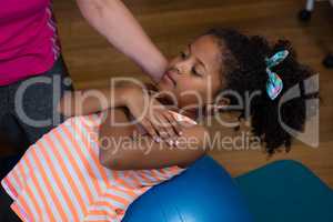 Female physiotherapist helping girl patient in performing exercise on fitness ball