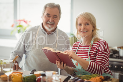 Smiling senior couple with recipe book standing in kitchen