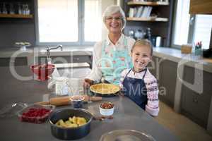 Smiling grandmother and granddaughter posing while making pie