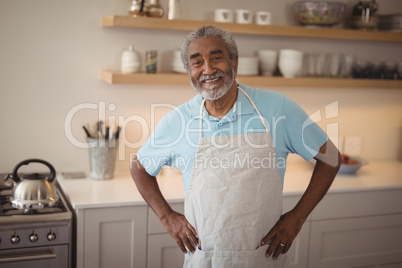 Smiling senior man standing with hand on hips in kitchen