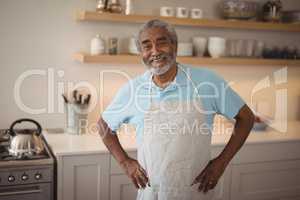 Smiling senior man standing with hand on hips in kitchen