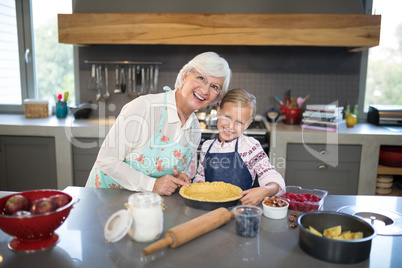 Smiling grandmother and granddaughter posing while making pie