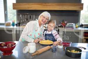 Smiling grandmother and granddaughter posing while making pie