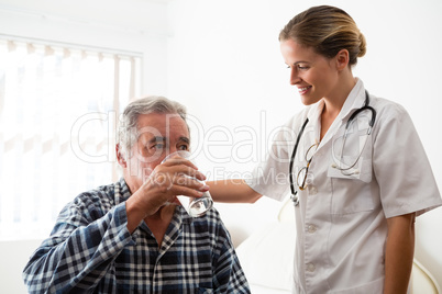 Female doctor standing by senior man drinking water