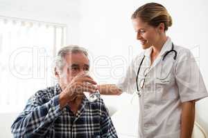Female doctor standing by senior man drinking water