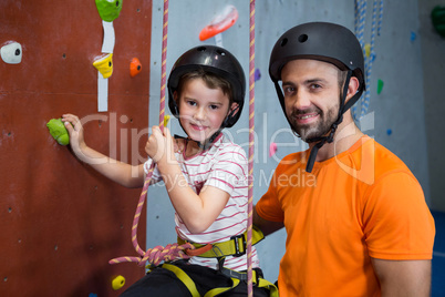 Trainer assisting boy in rock climbing at fitness studio