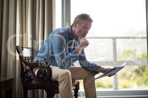 Man sitting on chair and reading newspaper in living room