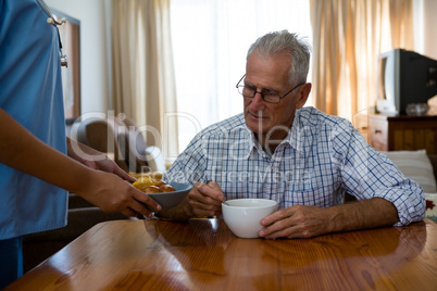 Female doctor serving food to senior man in nursing home