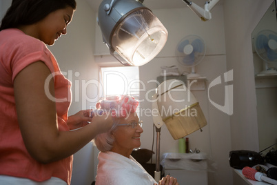 Side view of beautician adjusting curlers on senior woman hair