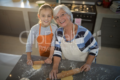 Grandmother and granddaughter posing while flattening dough