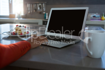 Cropped hand of woman using laptop at counter