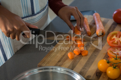 Mid section of woman cutting carrot in kitchen