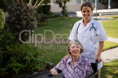 Portrait of doctor standing by senior woman sitting on wheelchair