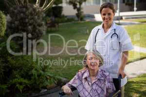 Portrait of doctor standing by senior woman sitting on wheelchair