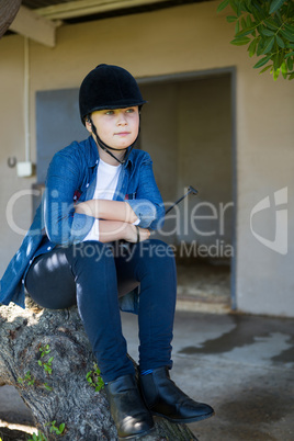 Girl sitting on tree trunk near stable