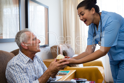 Senior man blowing candles of cup cake being held by female doctor
