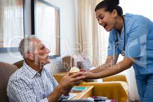 Senior man blowing candles of cup cake being held by female doctor