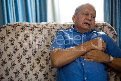 Thoughtful senior man looking away while sitting on sofa in nursing home