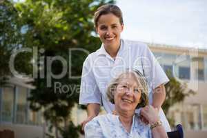 Smiling doctor standing by senior woman sitting on wheelchair