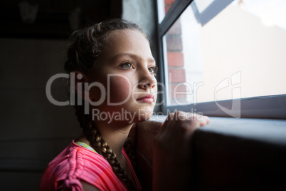 Thoughtful teenage girl looking through window