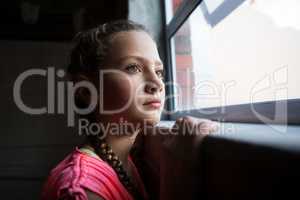 Thoughtful teenage girl looking through window