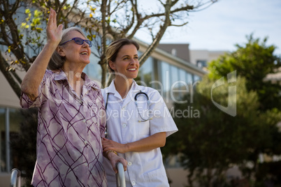 Senior woman waving hand while standing with doctor