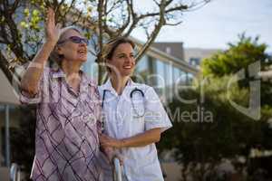 Senior woman waving hand while standing with doctor