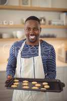 Smiling man holding tray of cookies in kitchen