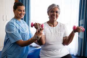 Nurse assisting senior woman in lifting dumbbells