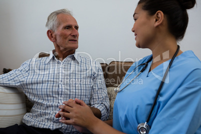Female doctor consoling senior man while sitting on sofa