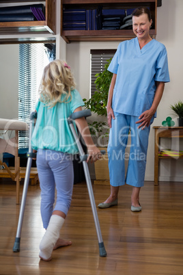 Physiotherapist assisting girl patient to walk with crutches