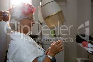 Cropped hands of hairstylist removing curlers from senior woman hair