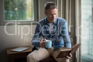 Man reading book while having coffee in living room