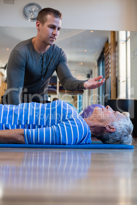 Physiotherapist assisting senior woman in performing exercise on mat