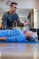 Physiotherapist assisting senior woman in performing exercise on mat