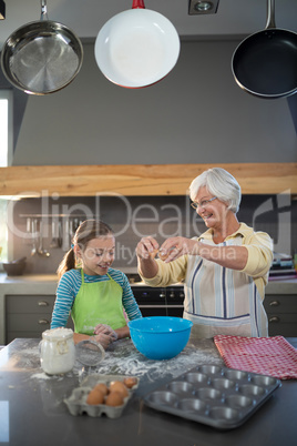 Smiling grandmother showing granddaughter to break eggs