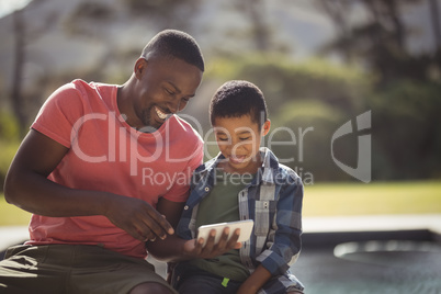 Son and father using mobile phone near poolside